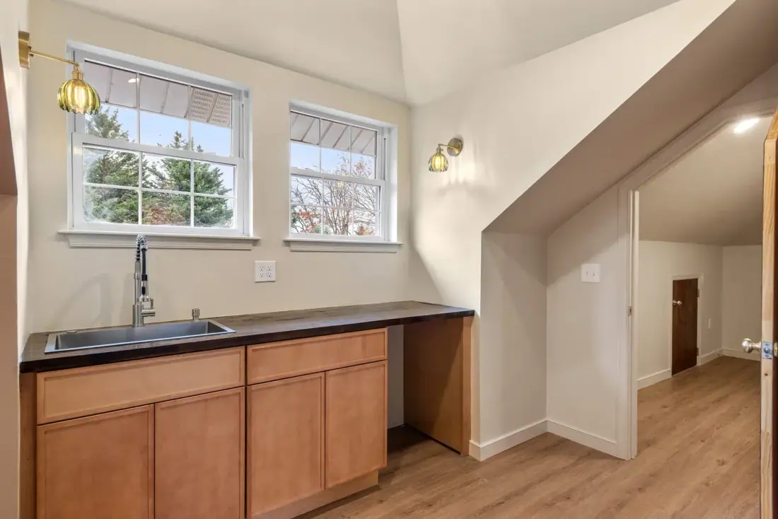 Attic kitchenette with wood cabinets and a dark countertop under a sloped ceiling