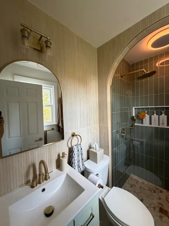 Arched shower entry with sage green vertical tile, brass fixtures and an arched mirror