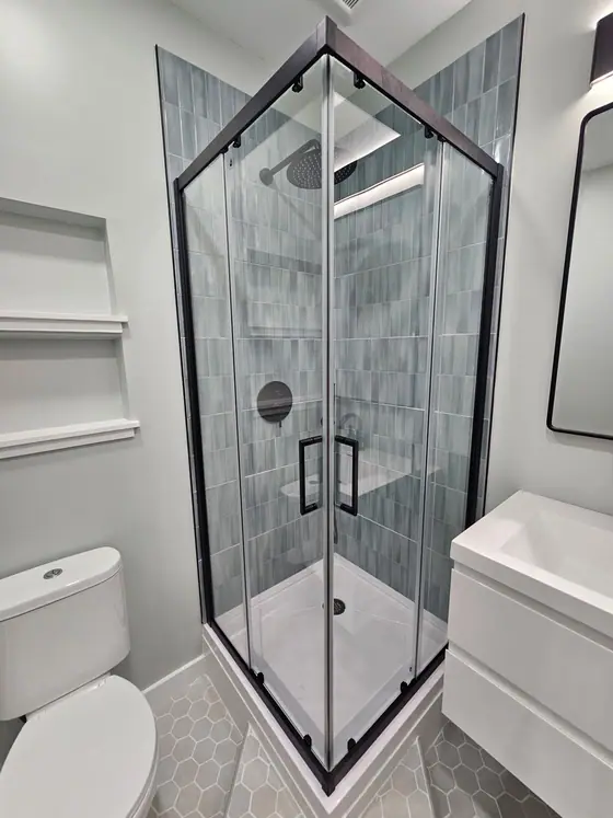 Corner shower with a black framed glass enclosure and blue gray vertical tile