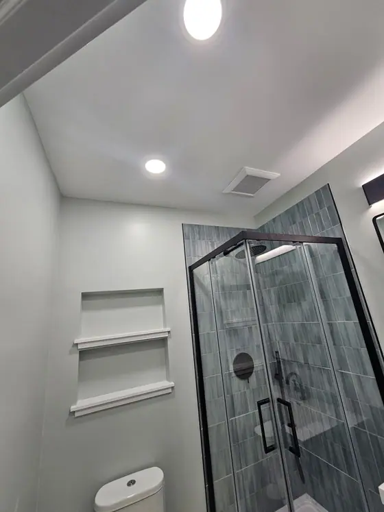 Small bathroom with a black framed corner shower and recessed wall shelves