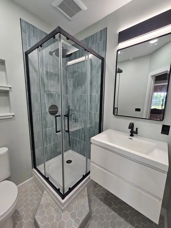 Black framed corner shower beside a white floating vanity and lit mirror