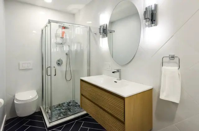Glass corner shower, wall hung toilet and a fluted wood vanity in a white bathroom