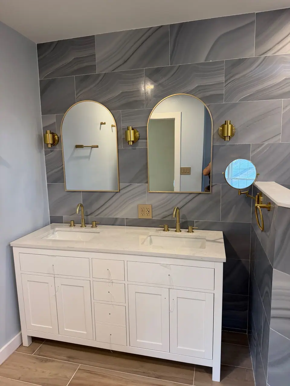 White double vanity with brass faucets and arched mirrors on a gray wave tile wall