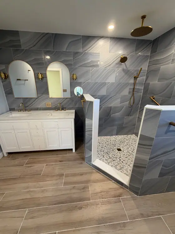 Walk in shower with pebble floor beside a white double vanity and wood look plank floor