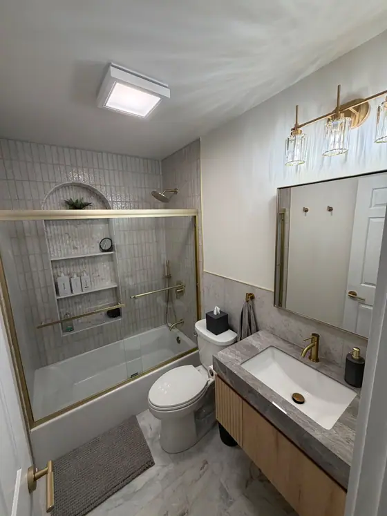 Bathroom with brass fixtures, a floating vanity and a glass enclosed tub with tile niche
