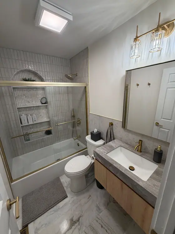 Remodeled hall bath with a brass vanity light, floating wood vanity and marble look floor tile