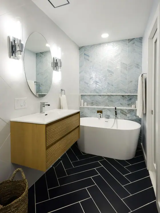 Freestanding tub, floating wood vanity and black herringbone floor tile