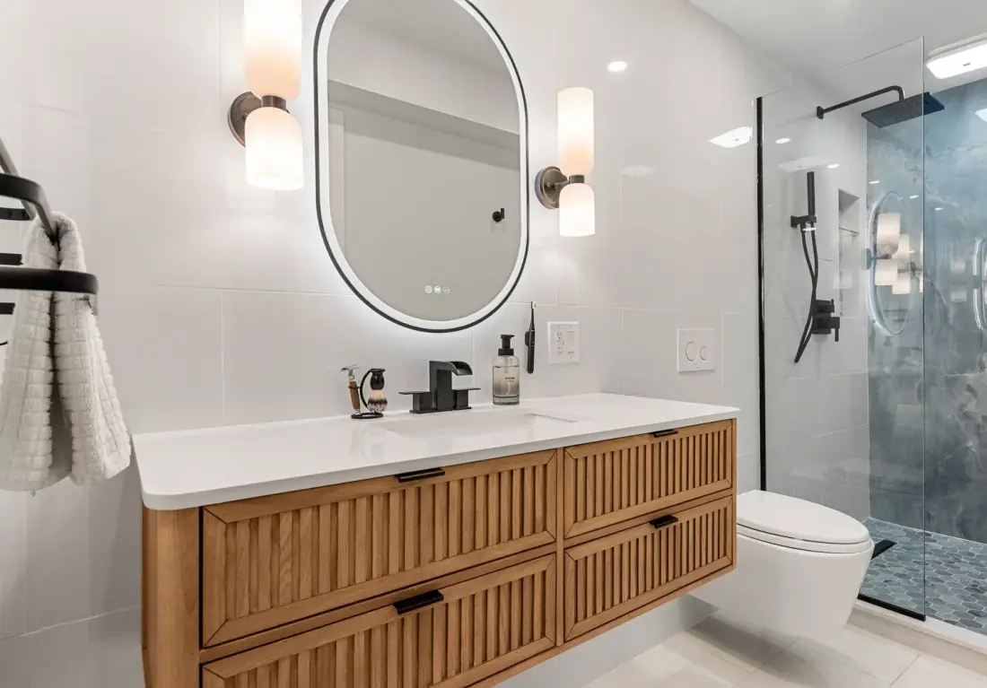 Floating wood vanity, oval LED mirror and wall hung toilet in a remodeled bathroom