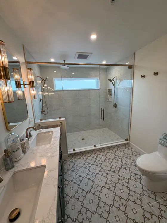 Long bathroom with a patterned cement look floor, double vanity and glass walk in shower
