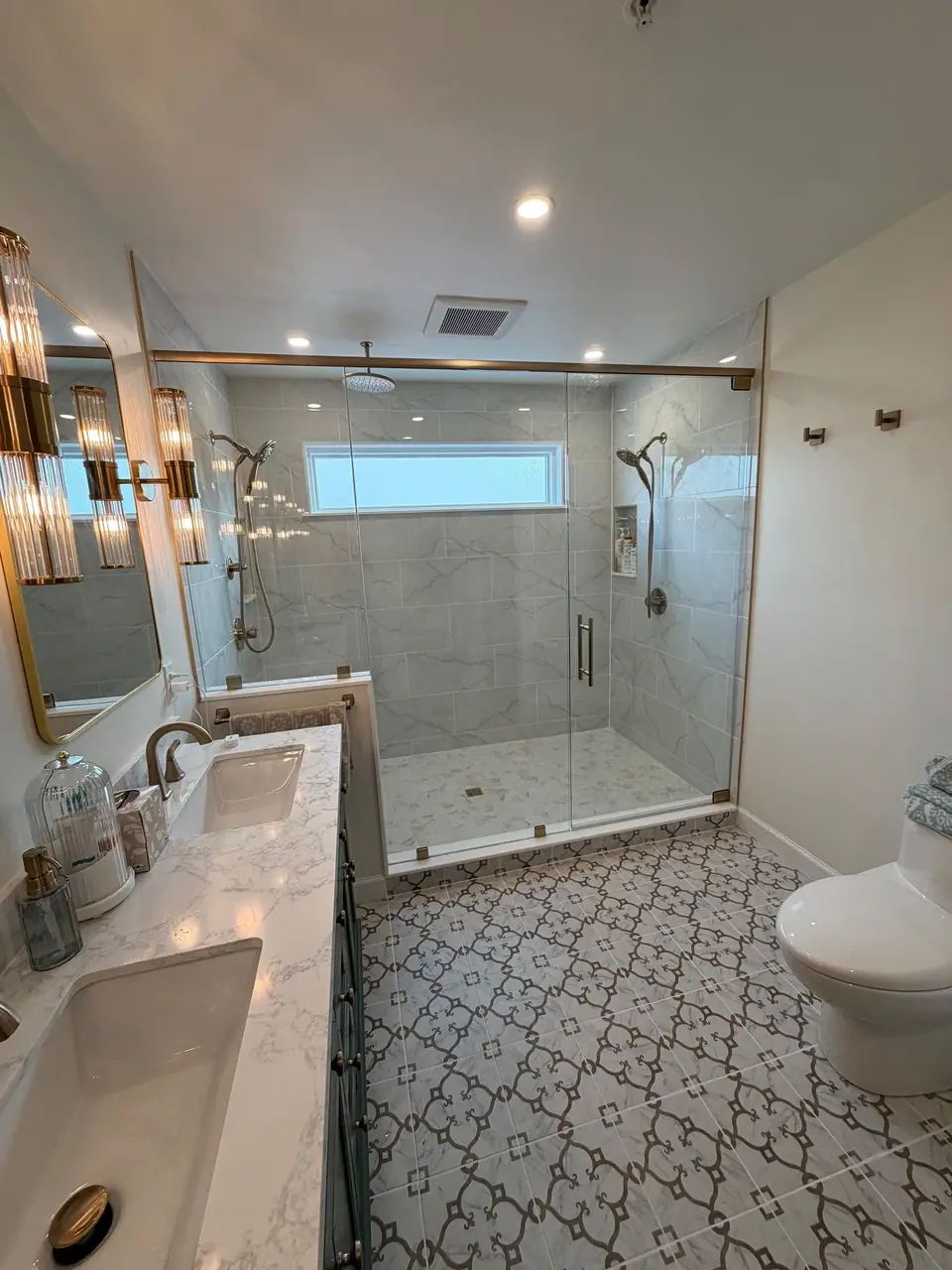 Long bathroom with a patterned cement look floor, double vanity and glass walk in shower
