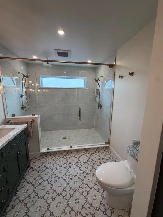 Walk in glass shower and dark green vanity over patterned floor tile