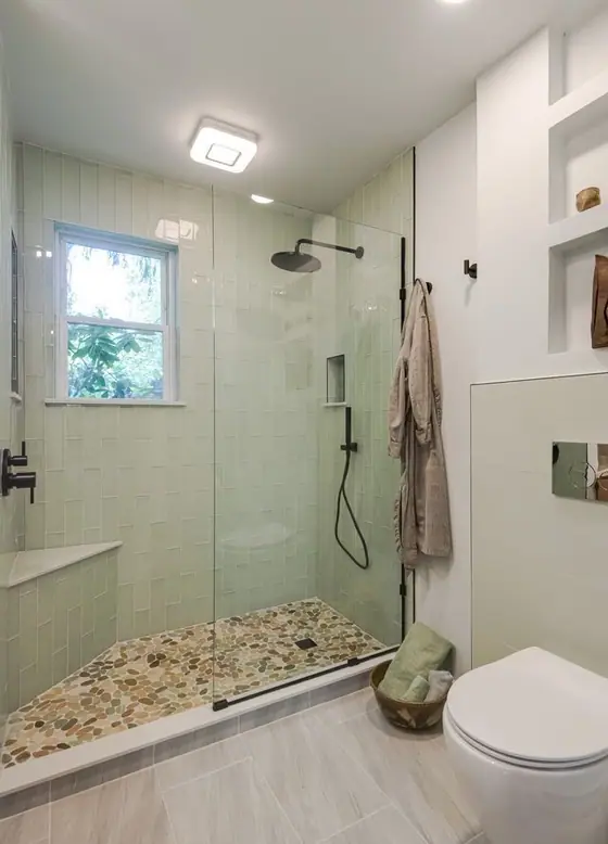 Glass walk in shower with a pebble floor, bench seat and pale green tile