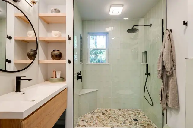Bathroom with built in wood shelves, a round mirror and a pebble floored walk in shower