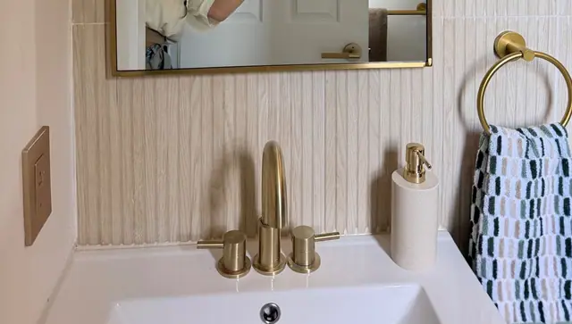 Brass faucet on a white sink against vertical cream tile