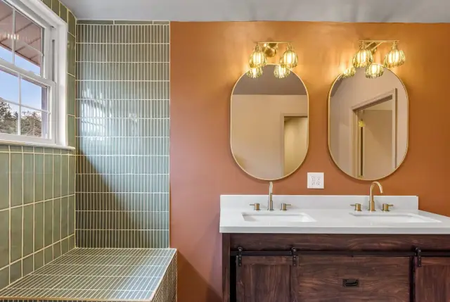 Double vanity bathroom with green stacked tile, terracotta walls and brass pendant sconces