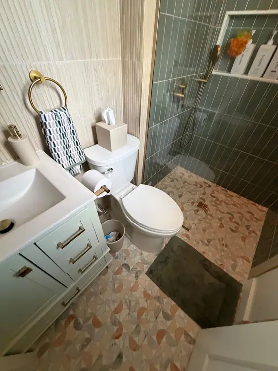 Bathroom with a colorful terrazzo style floor, sage green vanity and green tile shower