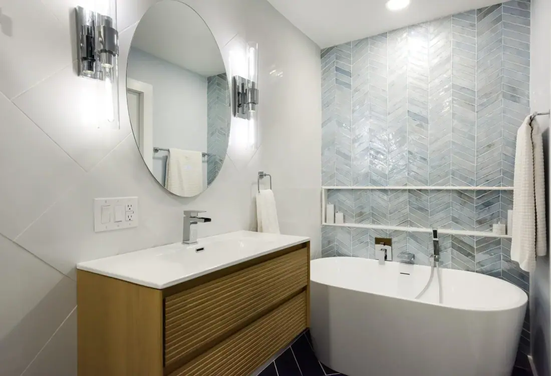 Bathroom with a freestanding tub, round mirror, wood vanity and blue chevron accent tile