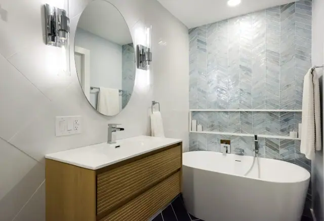 Bathroom with a freestanding tub, round mirror, wood vanity and blue chevron accent tile