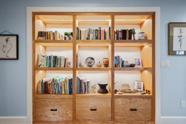 Built in wood bookcase with integrated lighting and lower drawers set into a blue wall