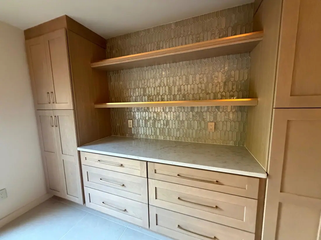 Light wood cabinetry wall with floating shelves and a shimmering mosaic tile backsplash