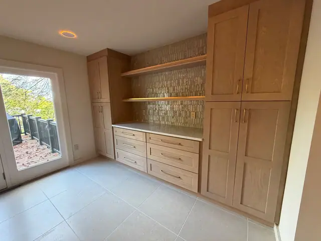 Built in light wood cabinets and open shelves along a wall beside patio doors