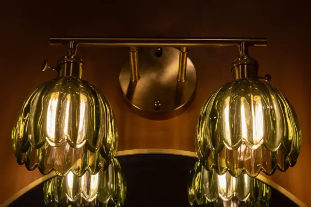 Brass vanity light with scalloped glass shades glowing against a terracotta wall