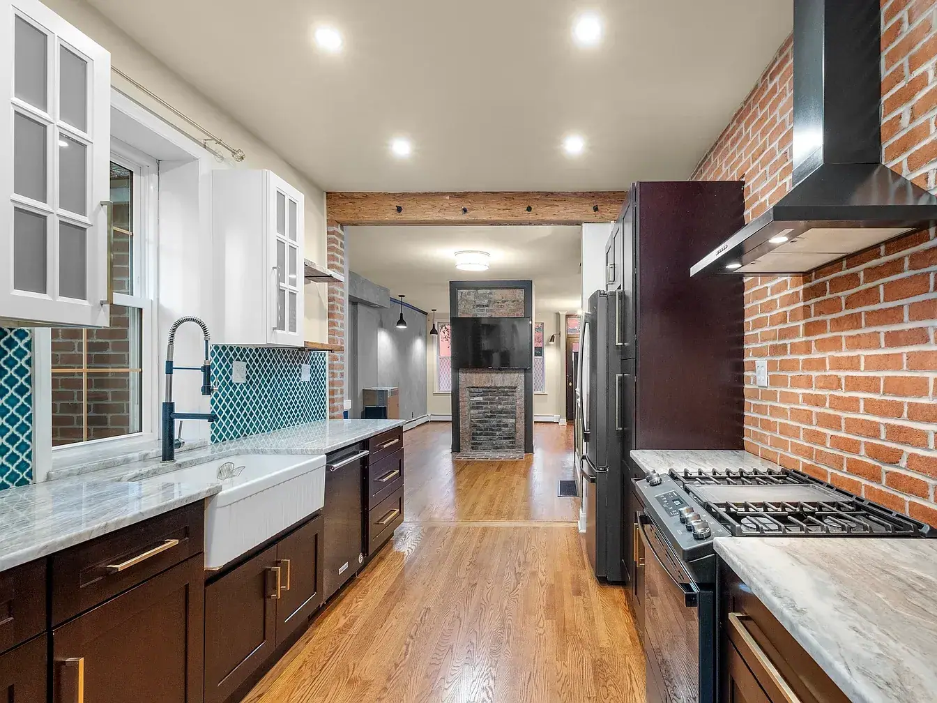 Galley kitchen remodel with dark shaker cabinets, a white farmhouse sink, exposed brick wall and black range hood