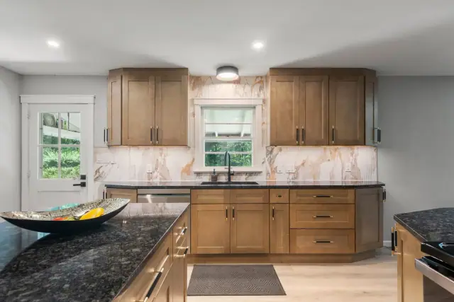Granite topped kitchen island facing a wall of wood cabinets with under cabinet lighting