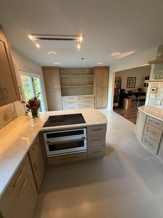 Light wood kitchen with a peninsula cooktop, built in wall ovens and large format floor tile