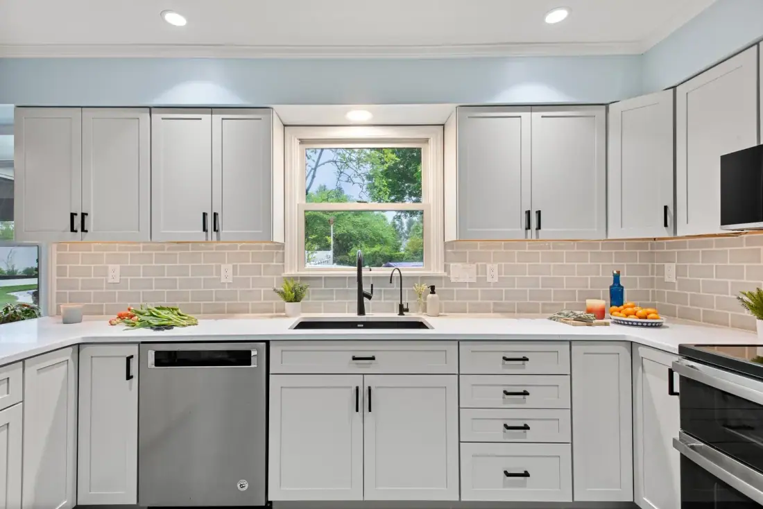 White kitchen cabinets and quartz counters around a window over the sink
