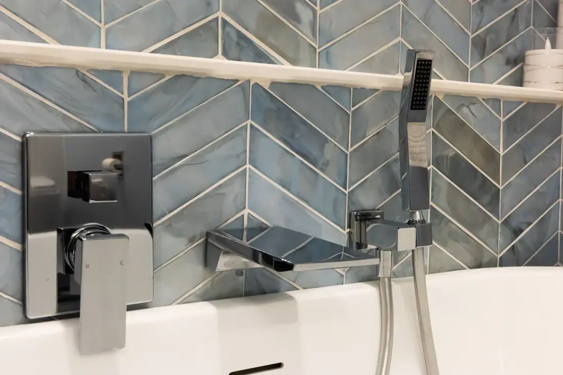 Glossy blue chevron tile behind a chrome tub filler and handheld shower
