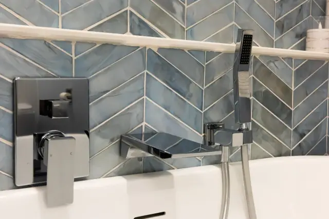 Glossy blue chevron tile behind a chrome tub filler and handheld shower